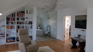Un salon moderne avec une grande bibliothèque, un fauteuil confortable, une cabine de douche en verre et une table à manger agrémentée d’un vase.