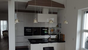 Une cuisine moderne avec des meubles blancs, des appareils électroménagers noirs et des luminaires suspendus.