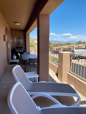 A covered outdoor area with a table and chairs, a grill, and a view of the surrounding landscape.
