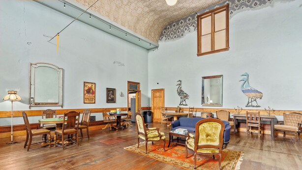 A spacious room with wooden floors, a dining area with chairs and a table, a sofa, and a large mirror.