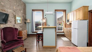 A compact kitchen with wooden cabinets, a built-in island, a flat-screen TV, and a stone wall.