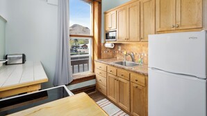 A compact kitchen with wooden cabinets, a built-in microwave, a stainless steel sink, and a white refrigerator.