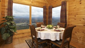 Un coin repas avec une table dressée pour quatre personnes, des murs en bois et de grandes fenêtres offrant une vue sur le paysage.