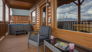 Une terrasse en bois avec un jacuzzi, une chaise et une table sur laquelle sont posés des magazines et une boisson.
