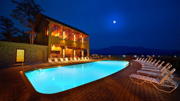 Un espace aménagé au bord de la piscine, avec des chaises longues et une piscine, un bâtiment doté de nombreuses fenêtres et une vue sur les montagnes.