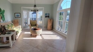 A sunlit room with a large window, a wicker chair, a small table with a basket, and a framed picture on the wall. - Paradise in Rehoboth.  Beautiful & spacious home -  August dates available. (Rehoboth)
