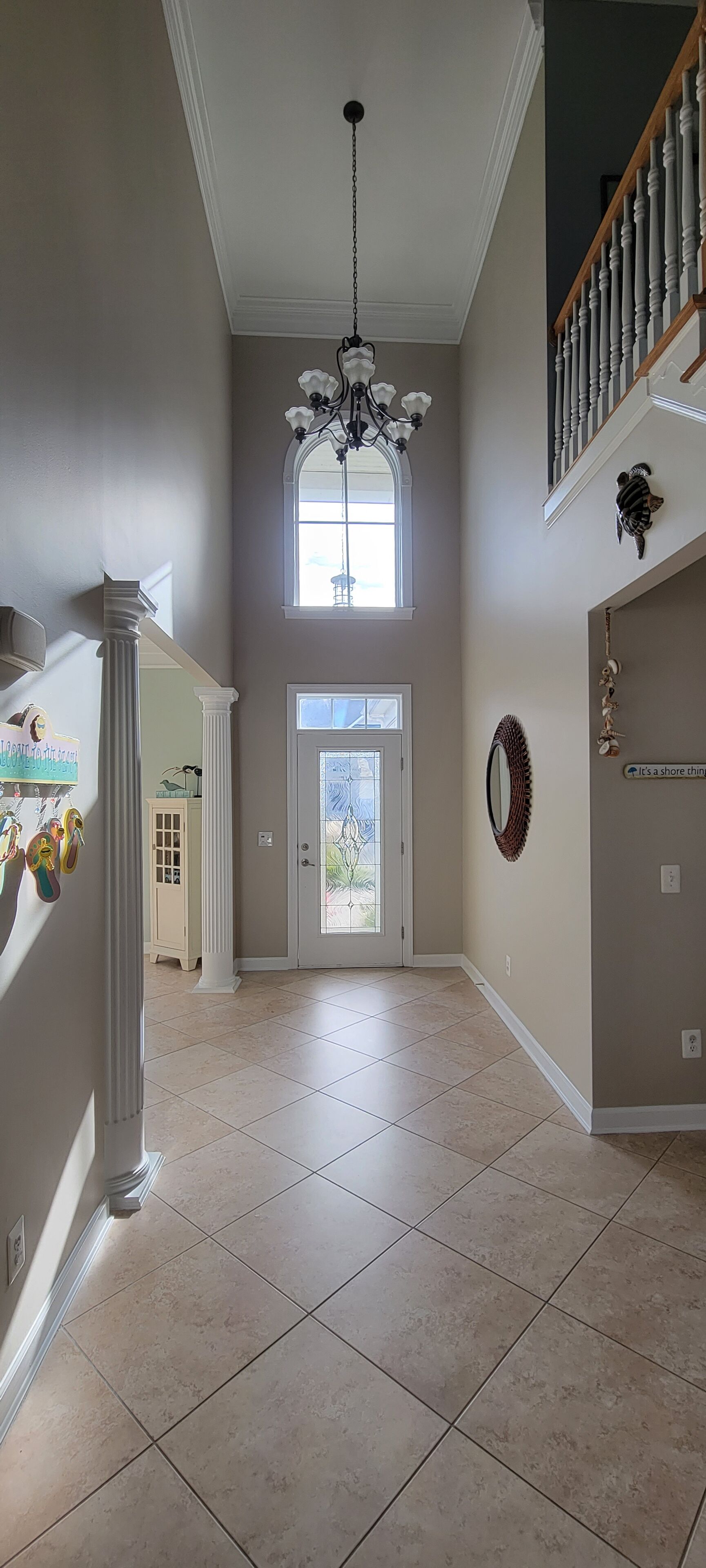 A spacious hallway with a chandelier, a large window, and a staircase.
