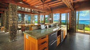 Una cocina con una isla grande, pilares de piedra y vistas al océano.