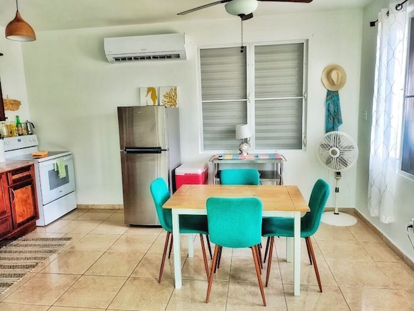 Une cuisine de taille réduite avec une table en bois et des chaises de couleur turquoise, un réfrigérateur en acier inoxydable et un ventilateur de plafond.