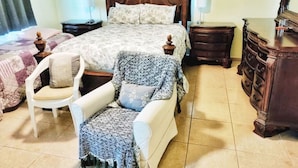 A bedroom with a large bed, a wooden dresser, a white armchair, and a patterned throw blanket. - Casa Menta in Rincon, Puerto Rico (Rincon)