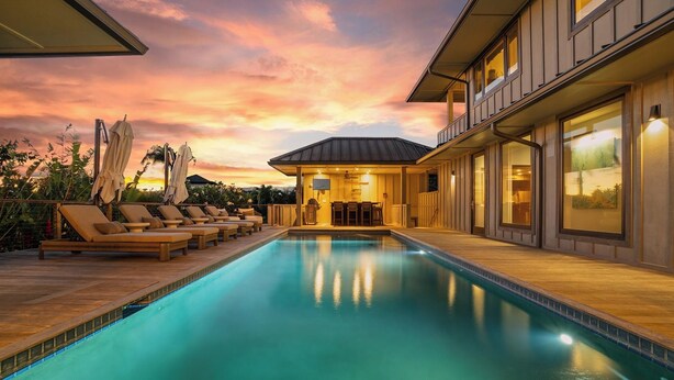 Una piscina con sillas de descanso, una zona de estar cubierta y vistas al atardecer.