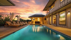 A swimming pool with lounge chairs, a covered seating area, and a view of the sunset.