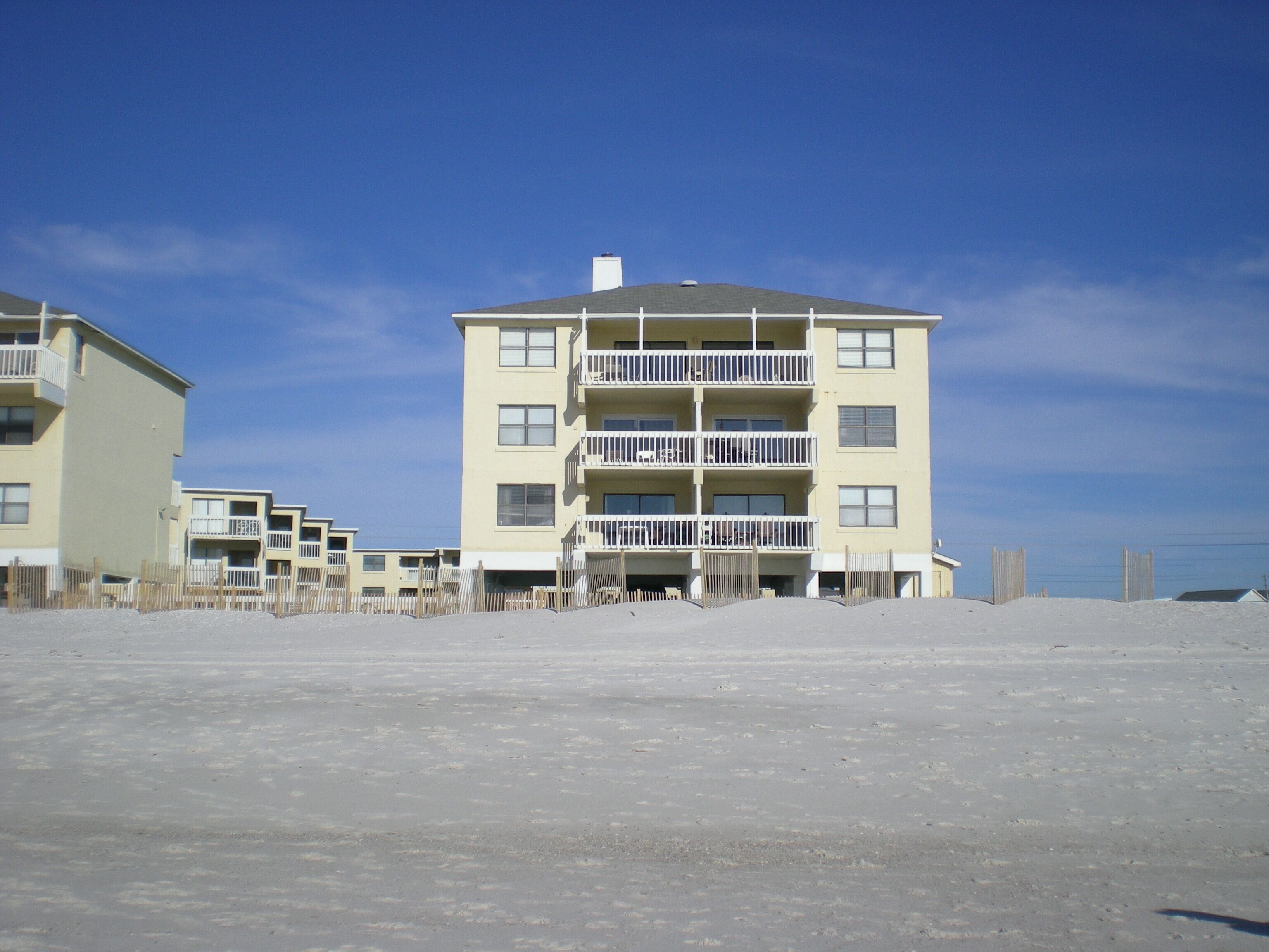 Un hotel de varios pisos con balcones y una playa de arena en primer plano.