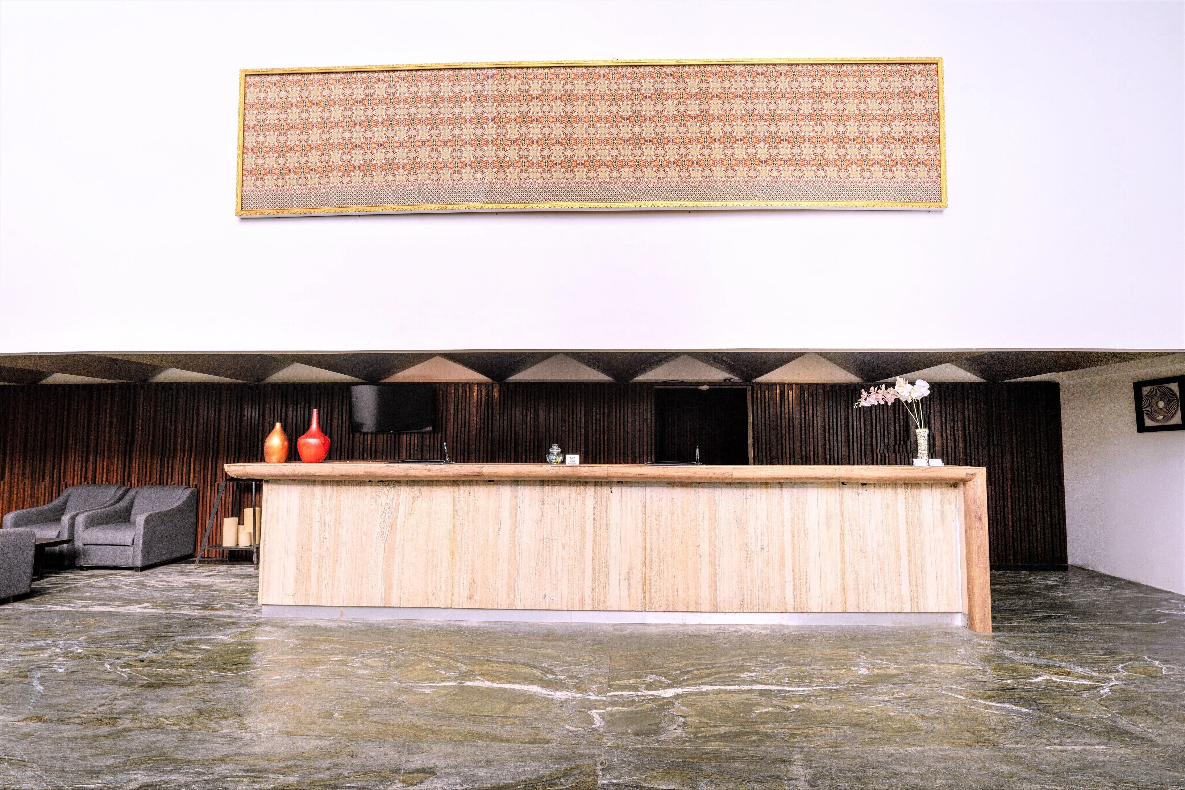 Un área de recepción con un mostrador de madera, un tapiz decorativo en la parte superior y un rincón de estar con un sofá y sillones.