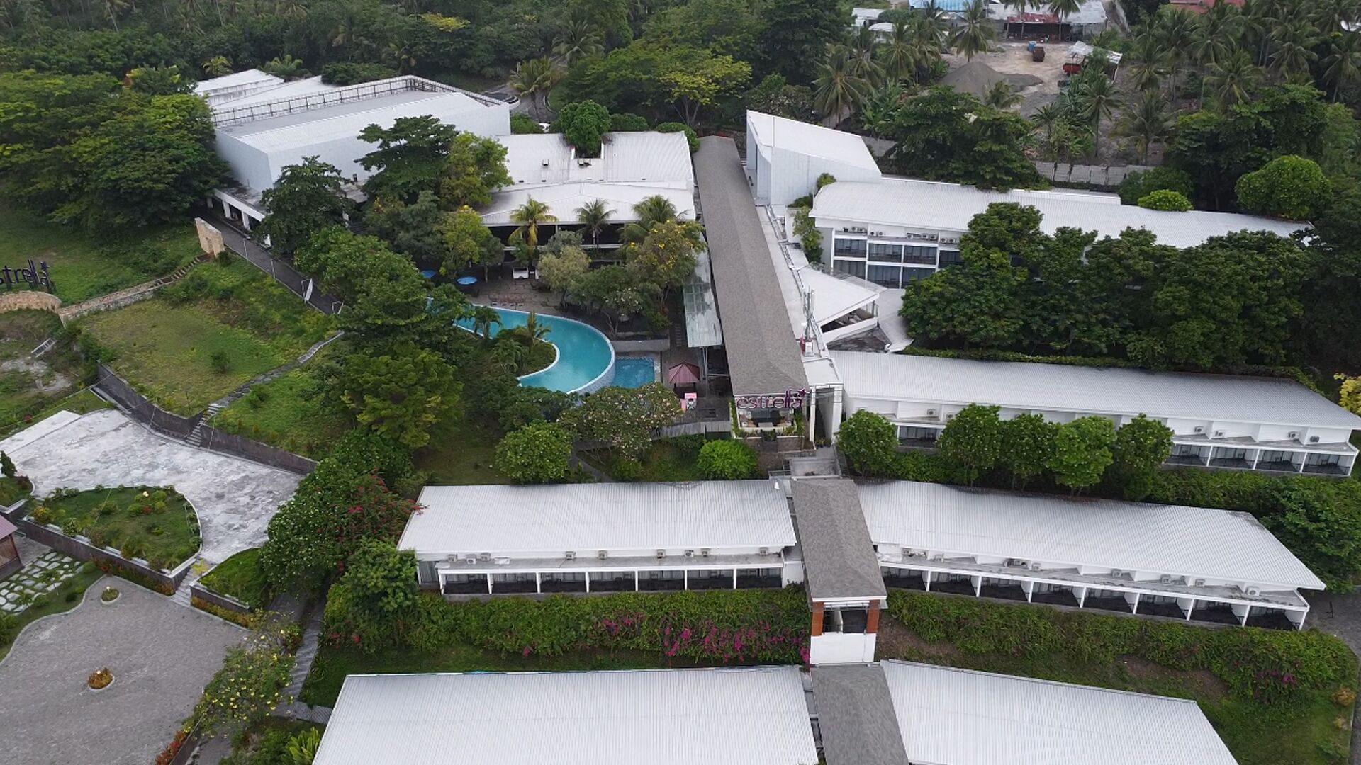 A large building with multiple white-roofed sections, a swimming pool, and surrounding greenery.