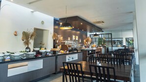A modern restaurant with a long counter, multiple seating areas, and a visible kitchen in the background. - Estrella Hotel & Conference (Luwuk)