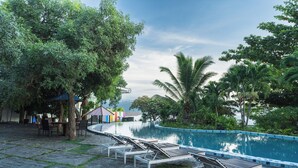 A pool area with lounge chairs, a covered seating area, and lush greenery. - Estrella Hotel & Conference (Luwuk)