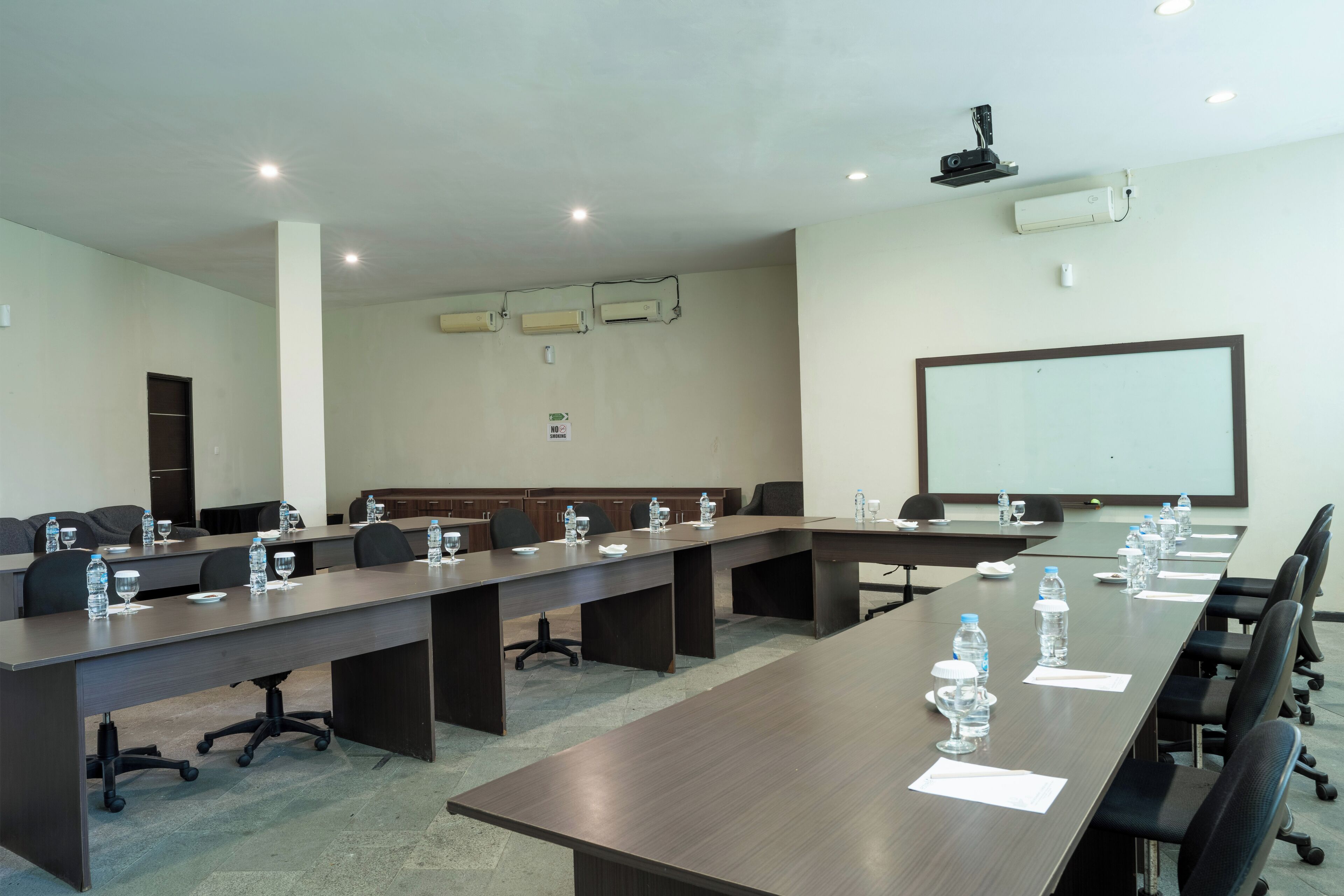 A conference room with long tables, chairs, water bottles, and a projector screen.
