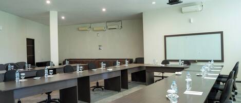 A conference room with long tables, chairs, water bottles, and a projector screen.
