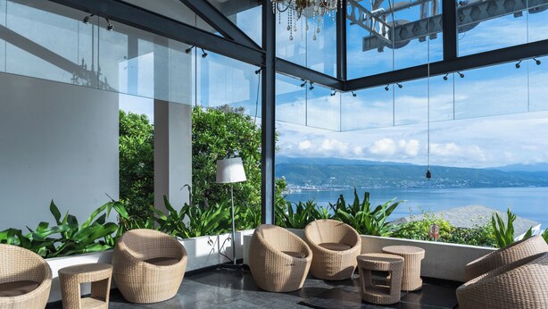 A modern outdoor seating area with wicker furniture and a view of the sea. - Estrella Hotel & Conference (Luwuk)