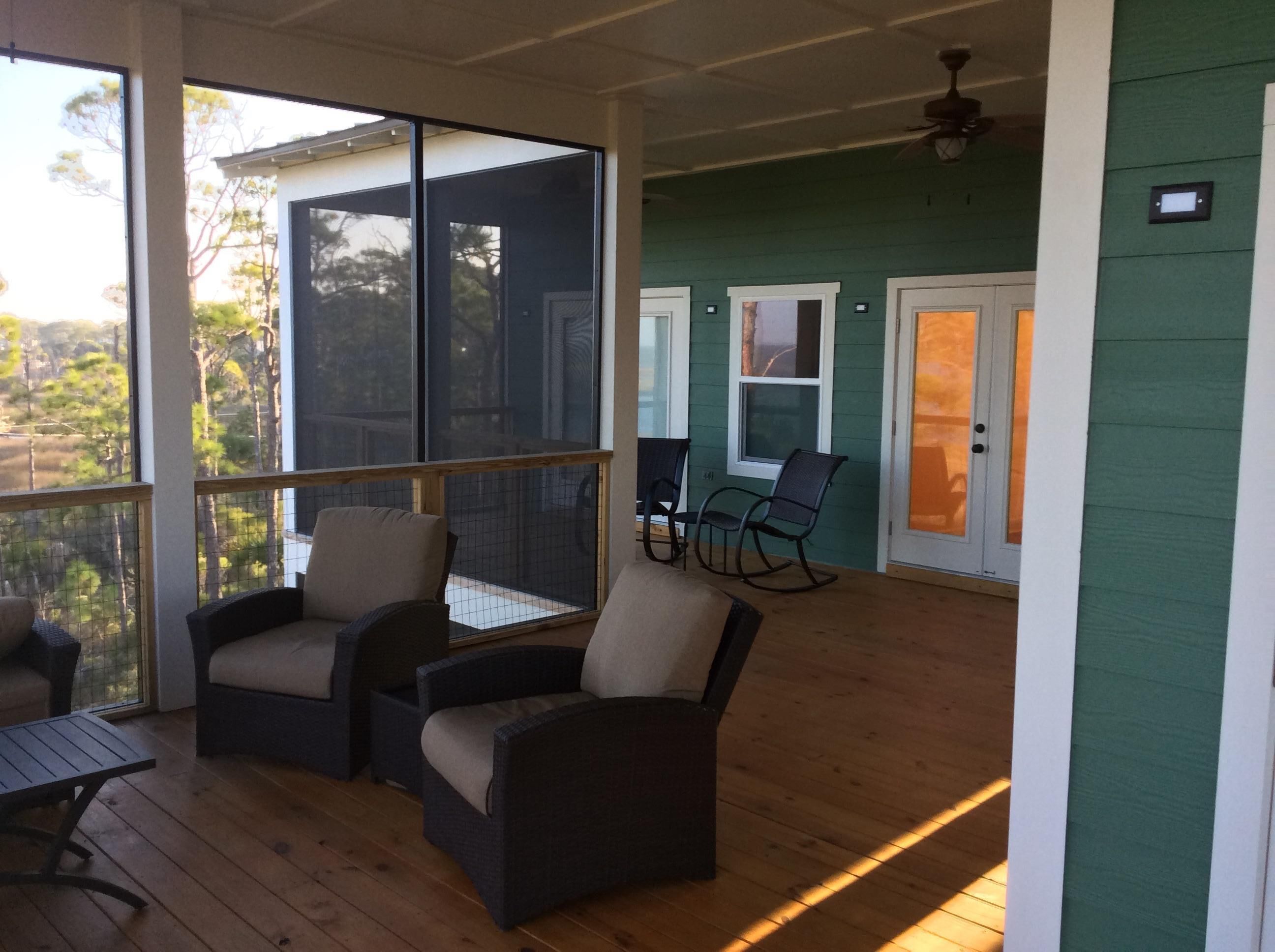 Eine überdachte Veranda mit Korbstühlen und einem Tisch, eine Schiebetür und Blick ins Freie.