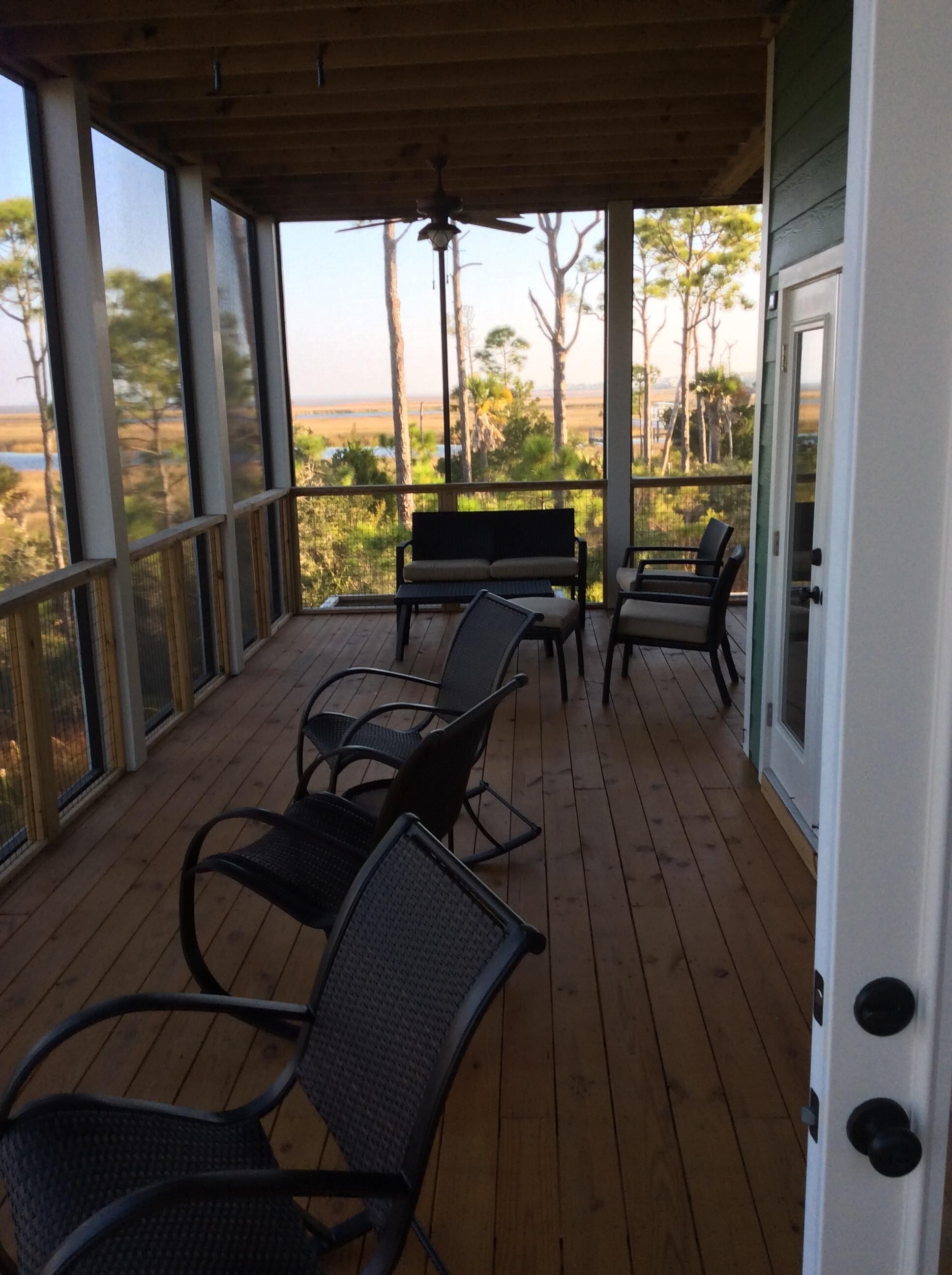 Ein überdachter Außenbereich mit Holzterrasse, mehreren Stühlen, einer Bank und Blick auf Strand und Bäume.