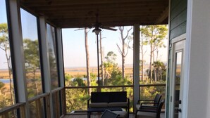 Ein überdachter Außenbereich mit Holzterrasse, mehreren Stühlen, einer Bank und Blick auf Strand und Bäume.