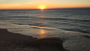 Ein Strand bei Sonnenuntergang, wobei sich die Sonne im Wasser spiegelt.