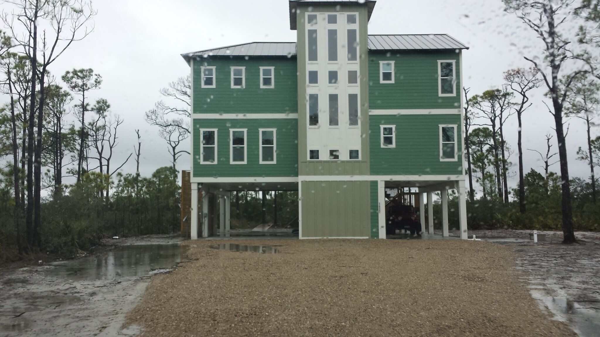 A two-story building with a central tower, surrounded by trees and a wet ground.