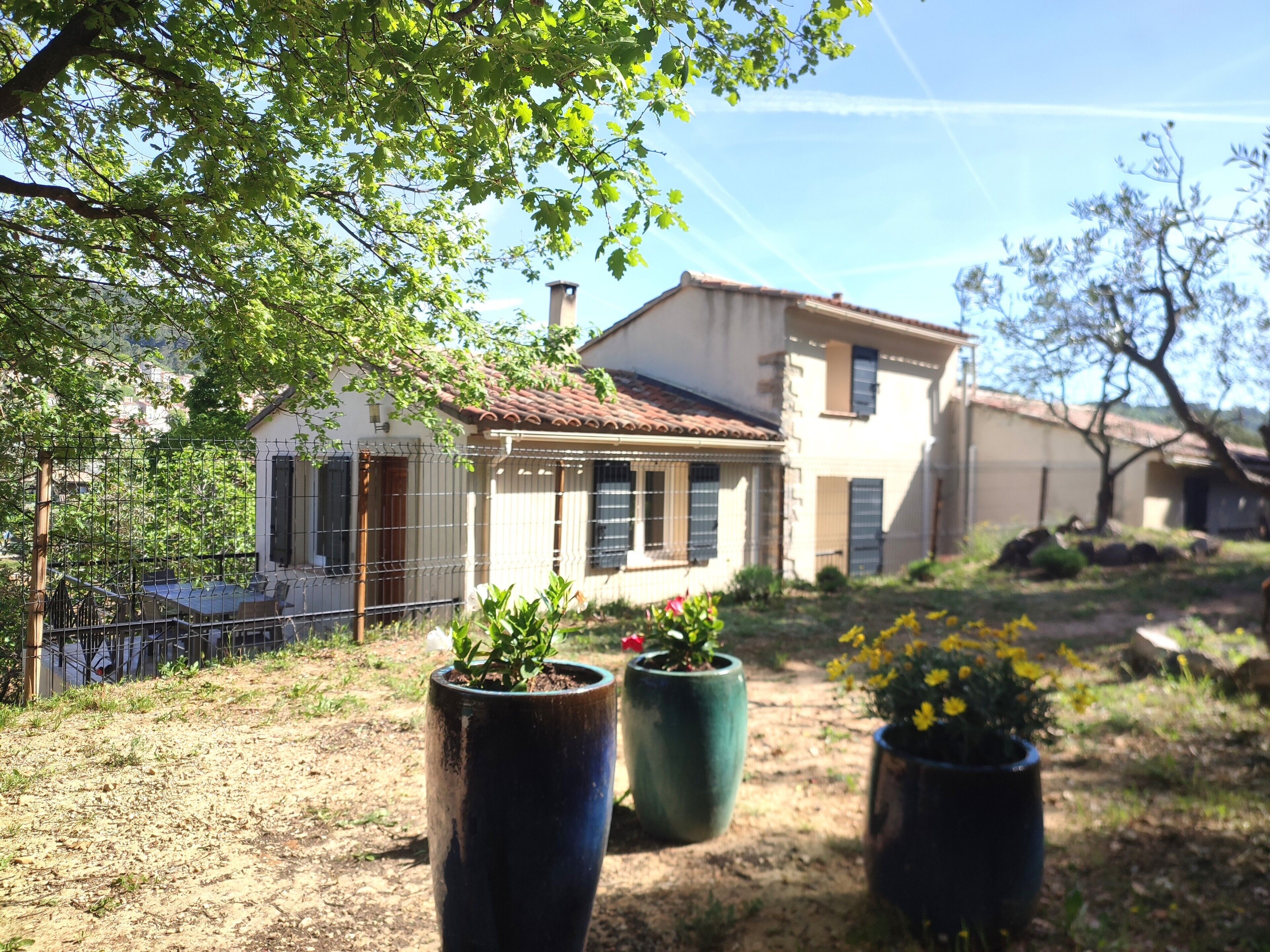 Une maison avec un jardin, une clôture et des plantes en pot.