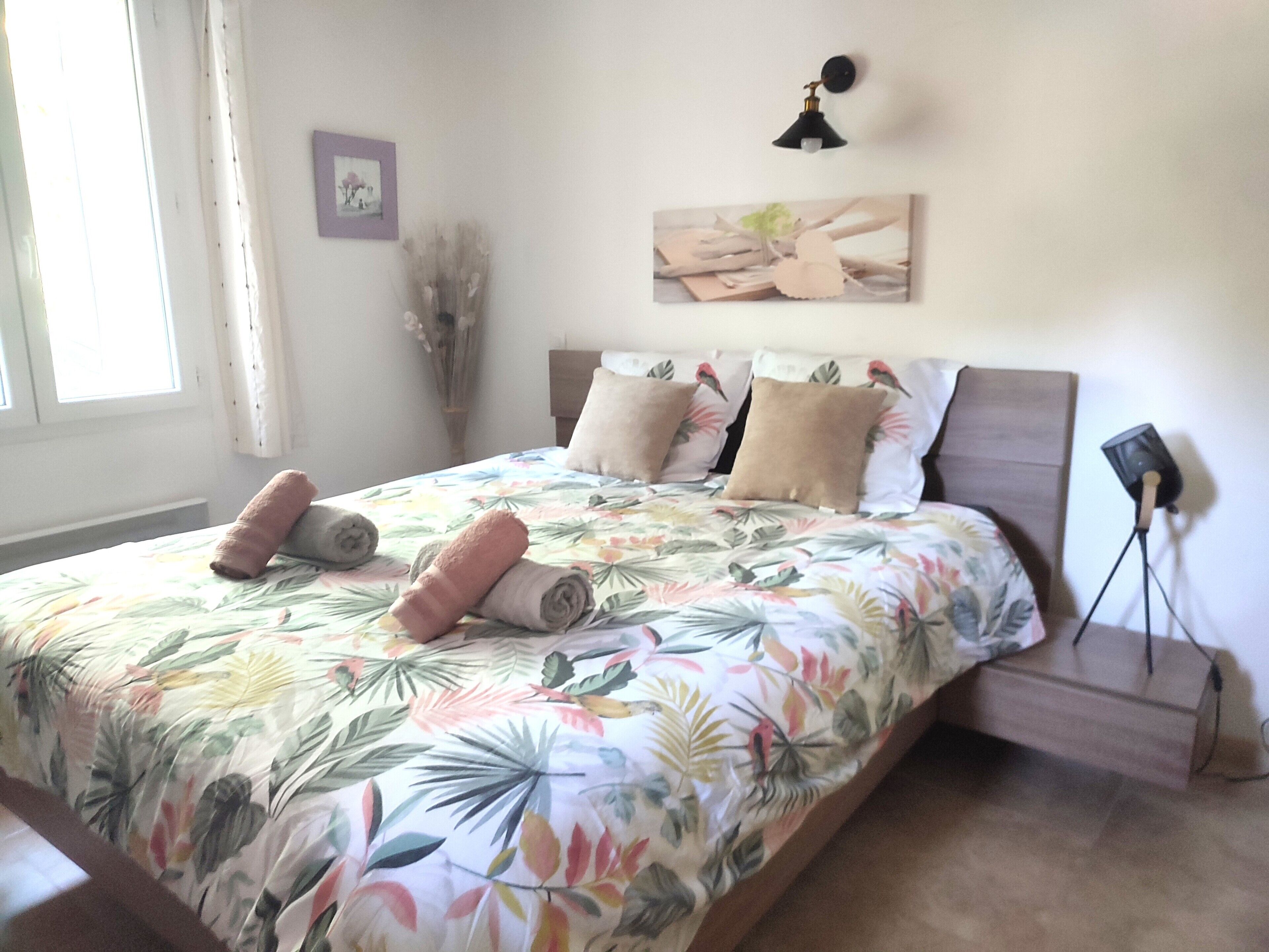 A bedroom with a bed, pillows, a nightstand, a lamp, and a wall-mounted picture.