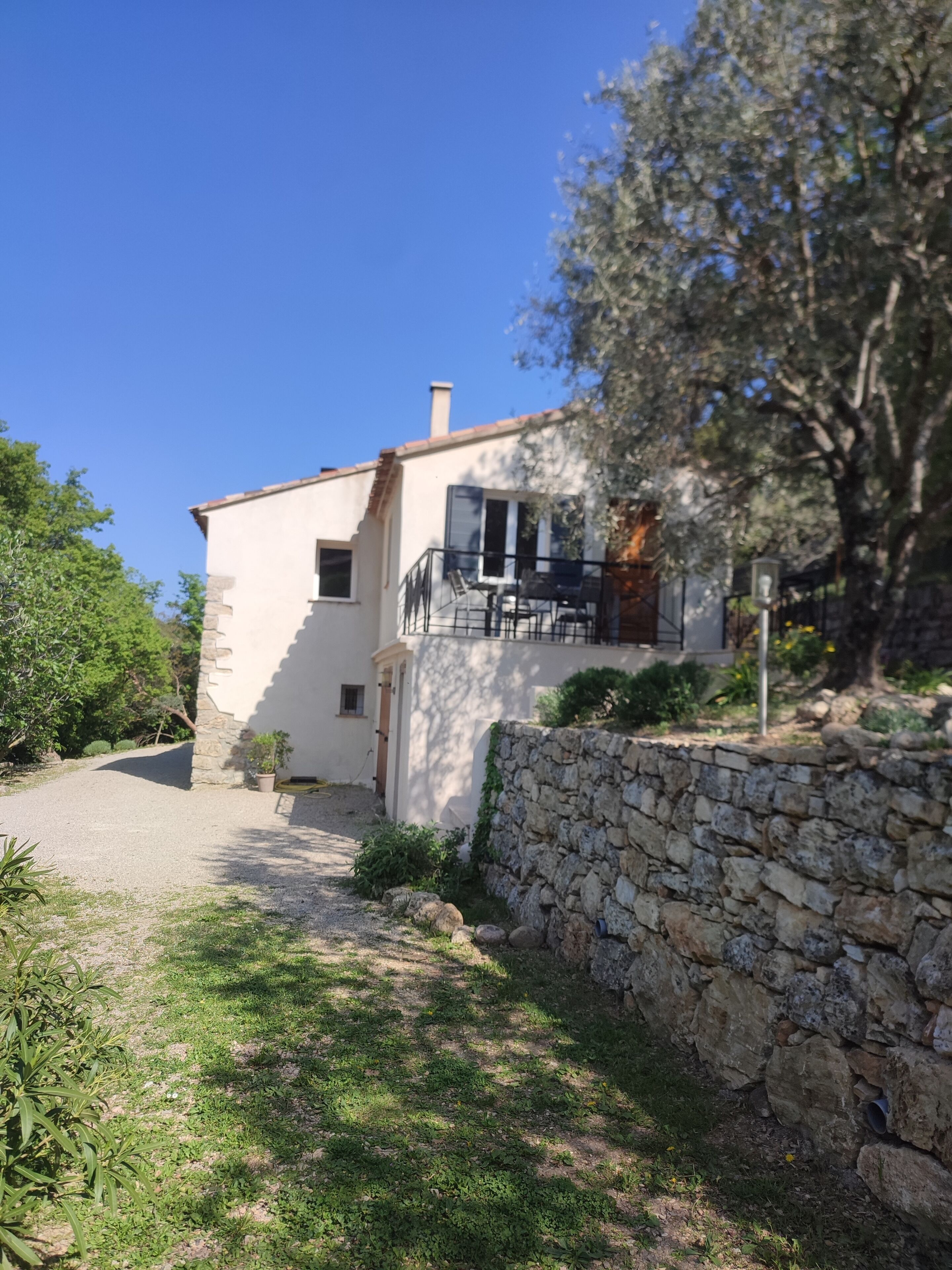 A two-story house with a stone wall, a balcony, and a garden path leading to the entrance.