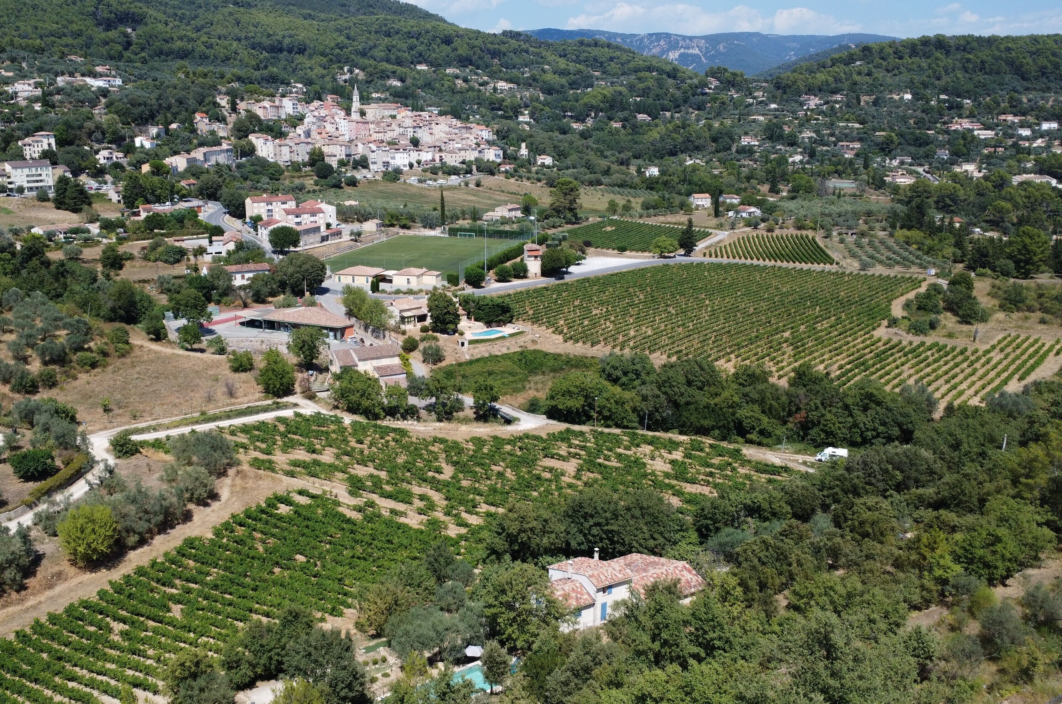 Vista aérea de uma cidade com vinhedos, uma igreja e edifícios residenciais.