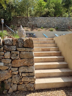 Una escalera de piedra que sube a una terraza con un muro de piedra y una estatua.