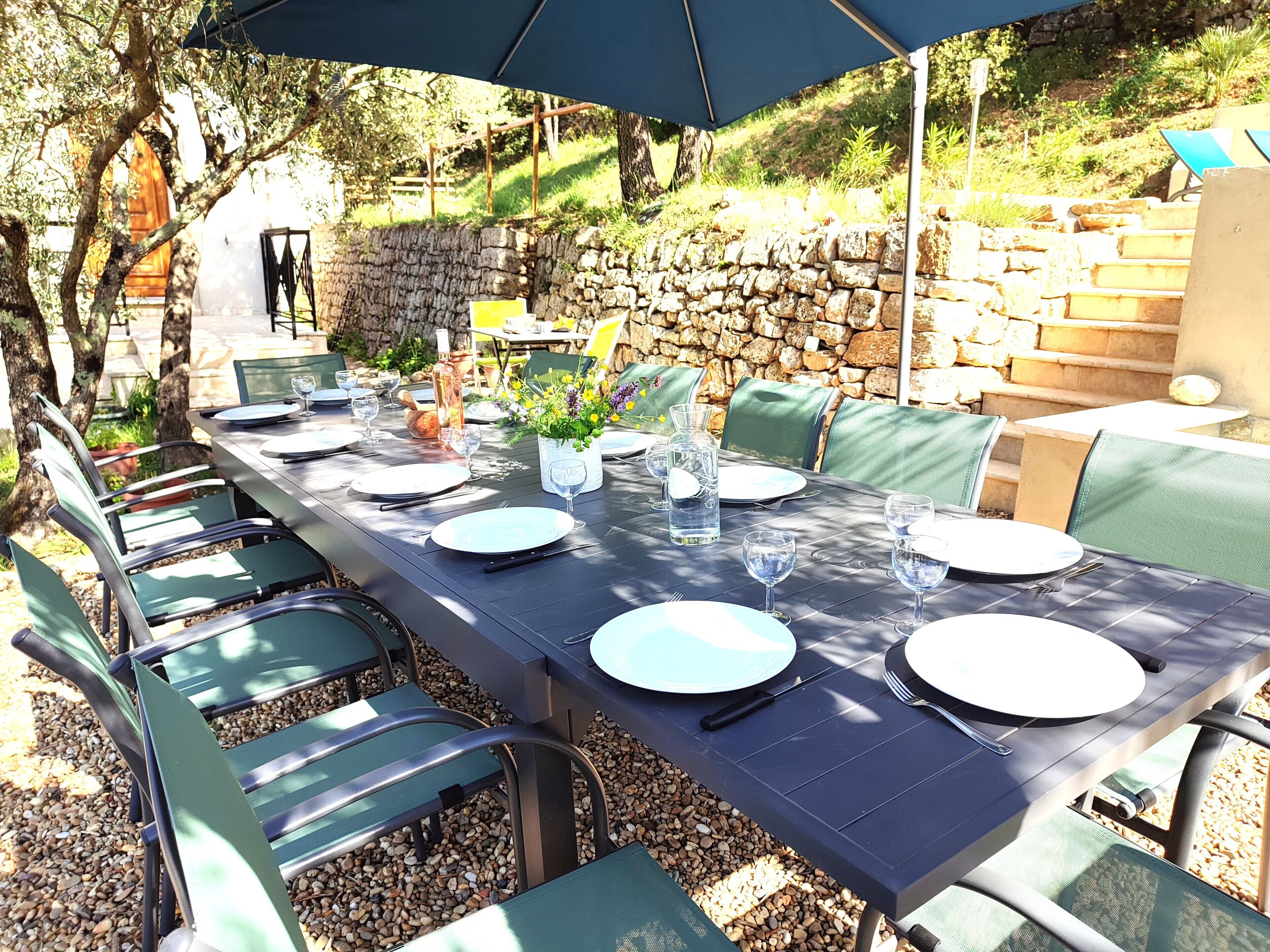 Un espacio de comedor al aire libre con un muro de piedra de fondo, sillas verdes y una mesa dispuesta para una comida.