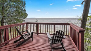Eine Holzterrasse mit zwei Adirondack-Stühlen, die auf ein Gewässer ausgerichtet sind.