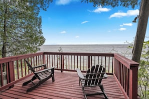A wooden deck with two Adirondack chairs facing a body of water.