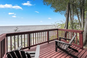A wooden deck with a railing overlooking a body of water, with chairs and a table.