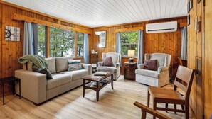 Ein Blockhaus-Interieur mit Holzvertäfelung, einer Couch, zwei Sesseln, einem Couchtisch und einem Holzstuhl.