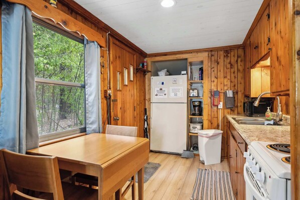 Una cocina compacta con paredes de madera, un refrigerador, una estufa y una zona de comedor con mesa y sillas.