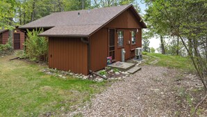 Eine kleine Holzhütte mit geneigtem Dach, einer Veranda und einer Schotterauffahrt.