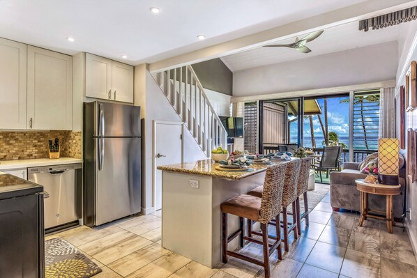 A modern kitchen with a stainless steel refrigerator, a built-in island with bar stools, and a staircase leading to a balcony with a view of the ocean. - Gorgeous Updated Oceanfront Condo 2BR /2BA AMAZING Molokai Views~Hale Honu (Lahaina)