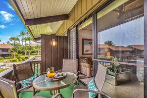 A balcony with a glass door, outdoor seating, and a view of the resort's landscape. - Gorgeous Updated Oceanfront Condo 2BR /2BA AMAZING Molokai Views~Hale Honu (Lahaina)