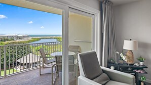 A balcony with a view of a body of water and a distant building, furnished with a chair, a table, and a lamp. - PARADISE + Incredible Views! Platinum Plus Escape – Islander 514 (Destin)