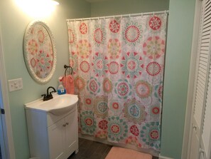 Une salle de bain avec un lavabo blanc, un miroir, un rideau de douche à motifs floraux et un mur de couleur vert clair.