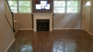 A spacious living room with a fireplace, large windows, and a staircase. - Cozy cottage in Sandy Pond (Pulaski)