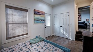 A bedroom with a bed, a window with blinds, a door, and a hallway leading to another room. - Charming One-Bedroom Unit in Historic Belhaven! (Jackson)