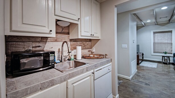 A kitchen with white cabinets, a black microwave, a sink, and a dish rack. - Charming One-Bedroom Unit in Historic Belhaven! (Jackson)