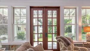 A room with a large wooden door, a cushioned sofa, and a patterned armchair. - Cedar Bluff Cabin in May in Old Town Bluffton on the river (Bluffton)