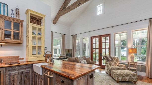 A spacious kitchen with wooden cabinets, a large island, and a dining area with a sofa and chairs. - Cedar Bluff Cabin in May in Old Town Bluffton on the river (Bluffton)